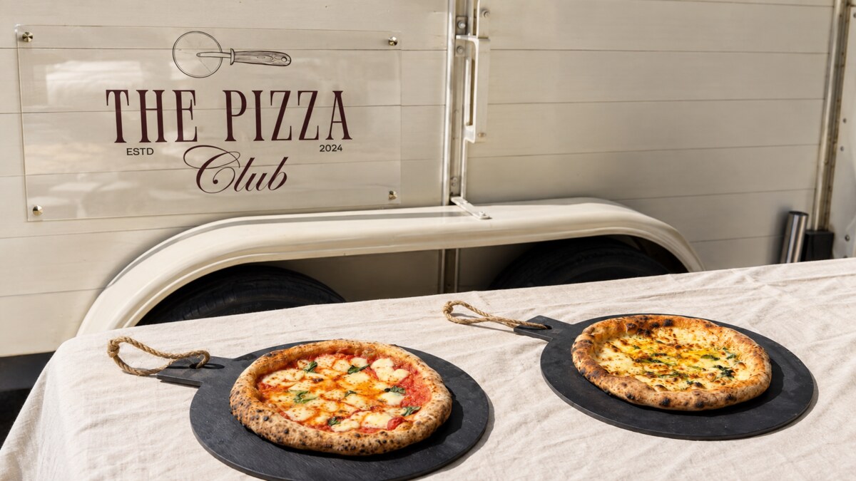 Two freshly baked pizzas set out in front of The Pizza Club trailer