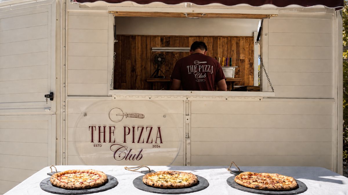 The Pizza Club horse trailer with Tom at the hatch and three wood-fired pizzas ready to serve